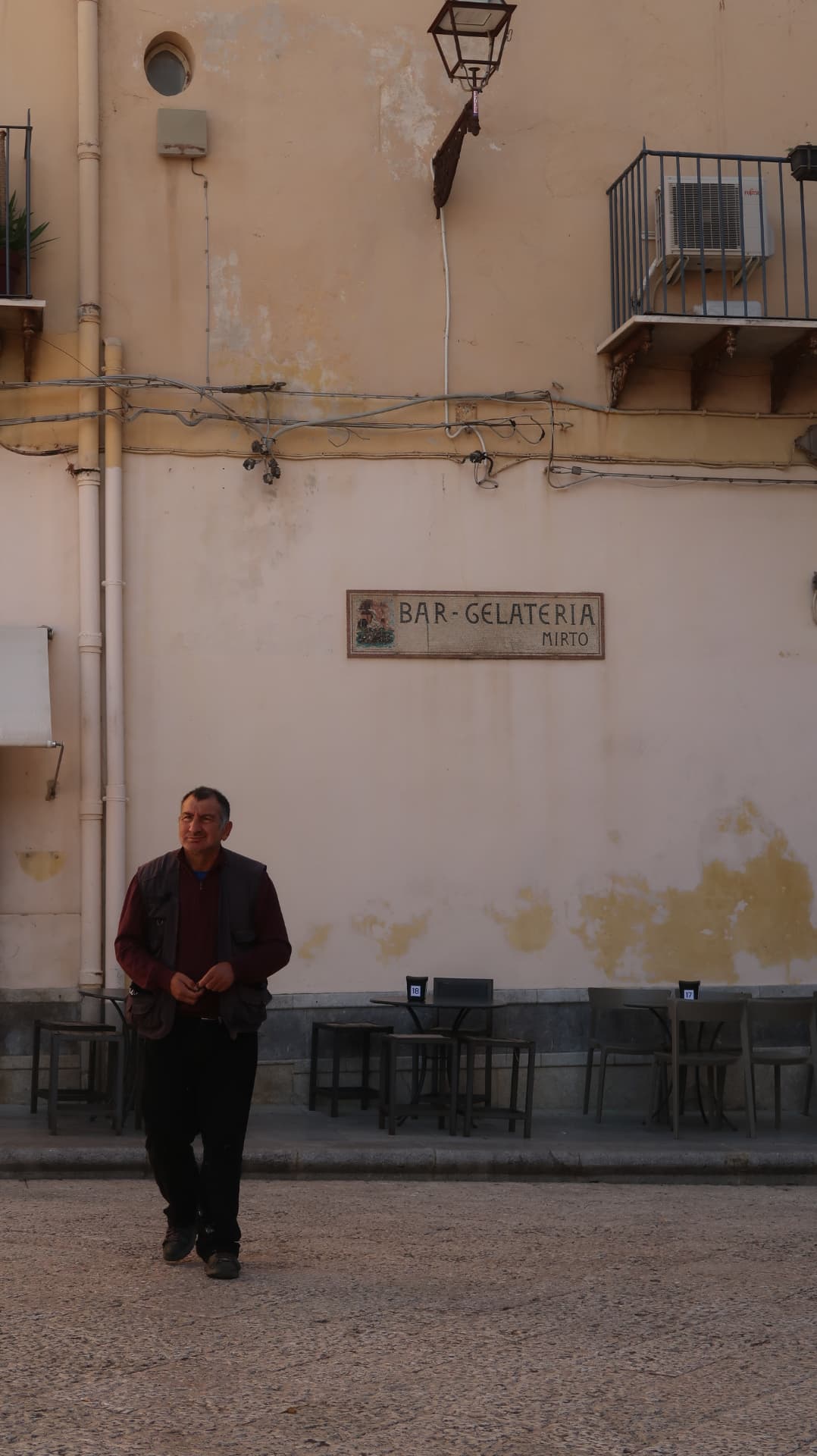 Man in a burgundy shirt walking past the Bar-Gelateria mosaic sign
