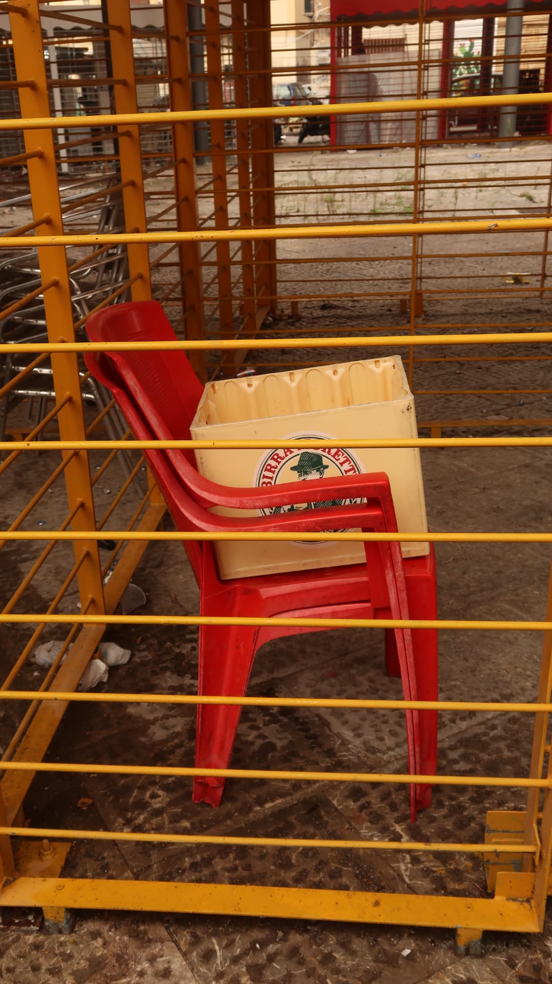 Stacked red and cream plastic chairs behind yellow market railings
