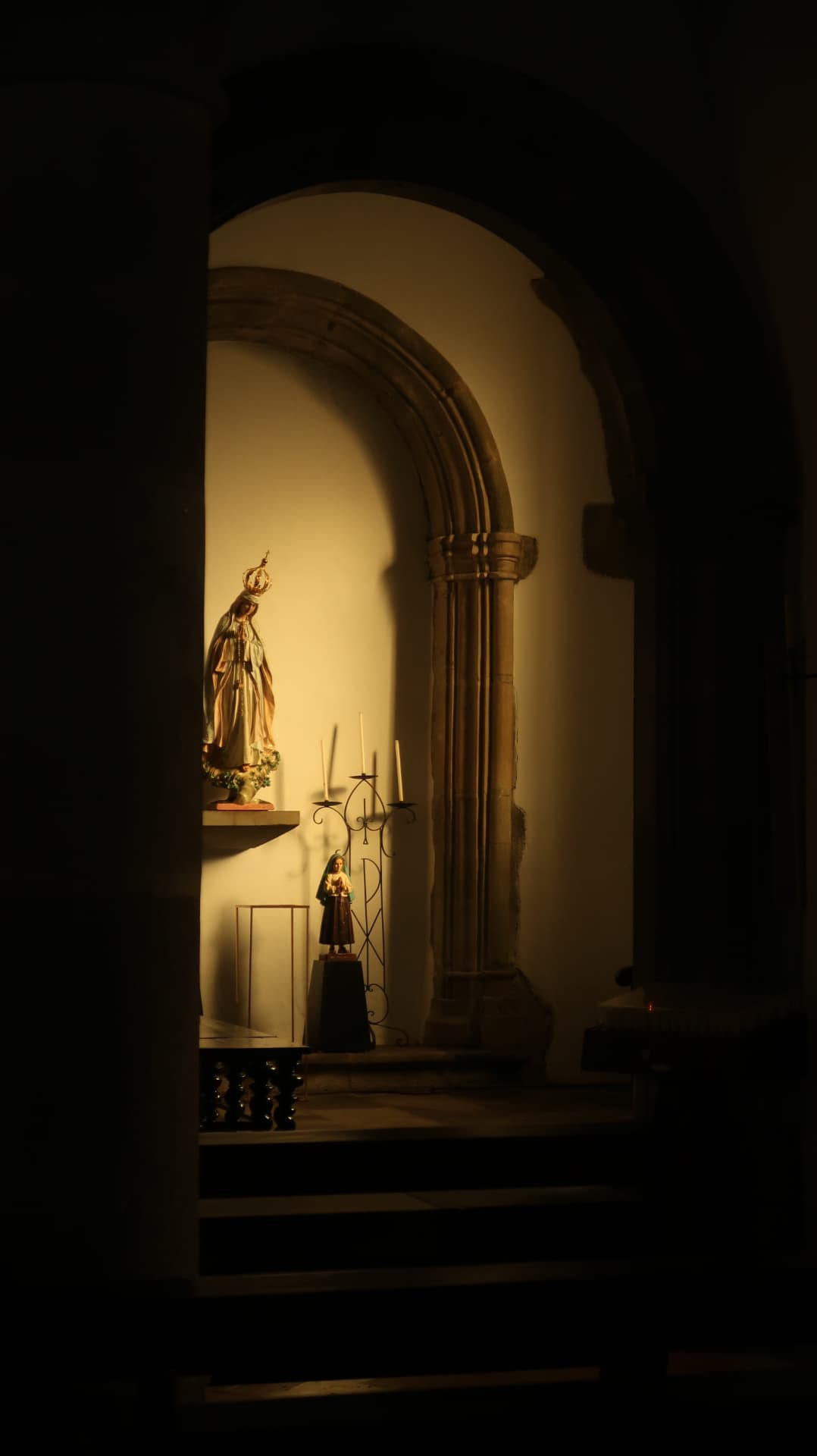 Lit chapel niche with statues seen through a dark arch