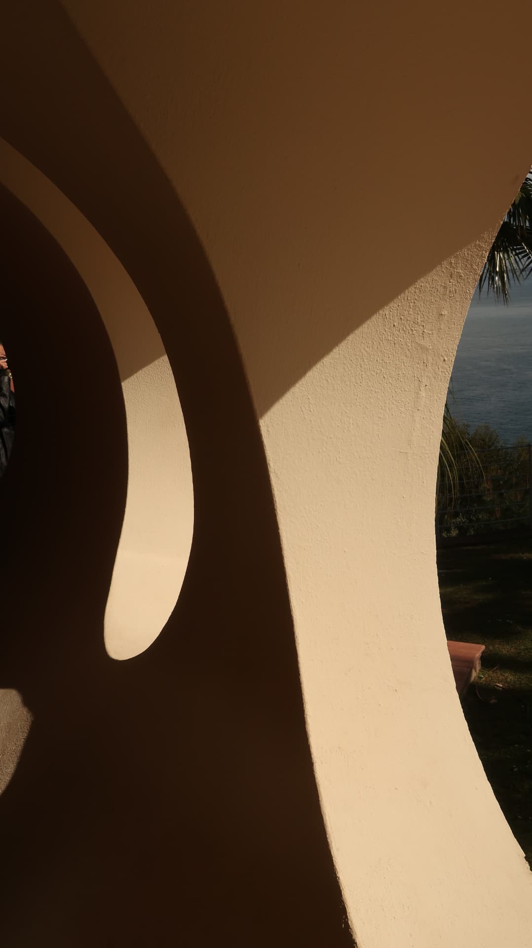 Curved exterior wall in raking sunlight with the sea beyond