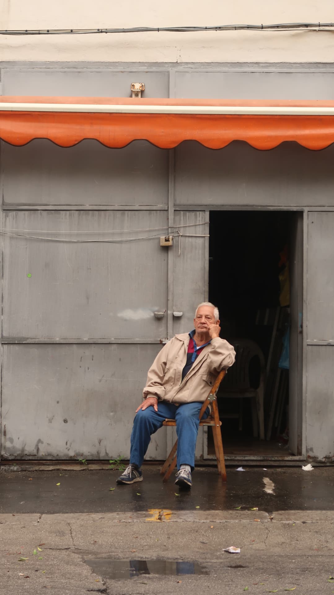 Man sitting on a folding chair under an orange scalloped awning