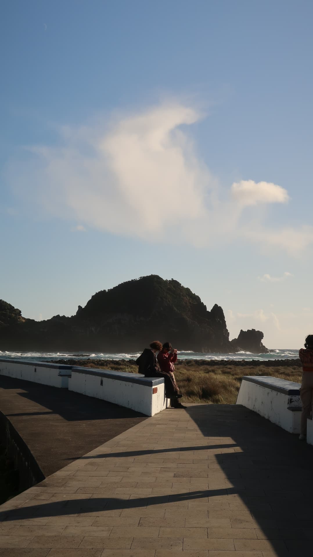 Figures sitting on a sea wall before a silhouetted headland