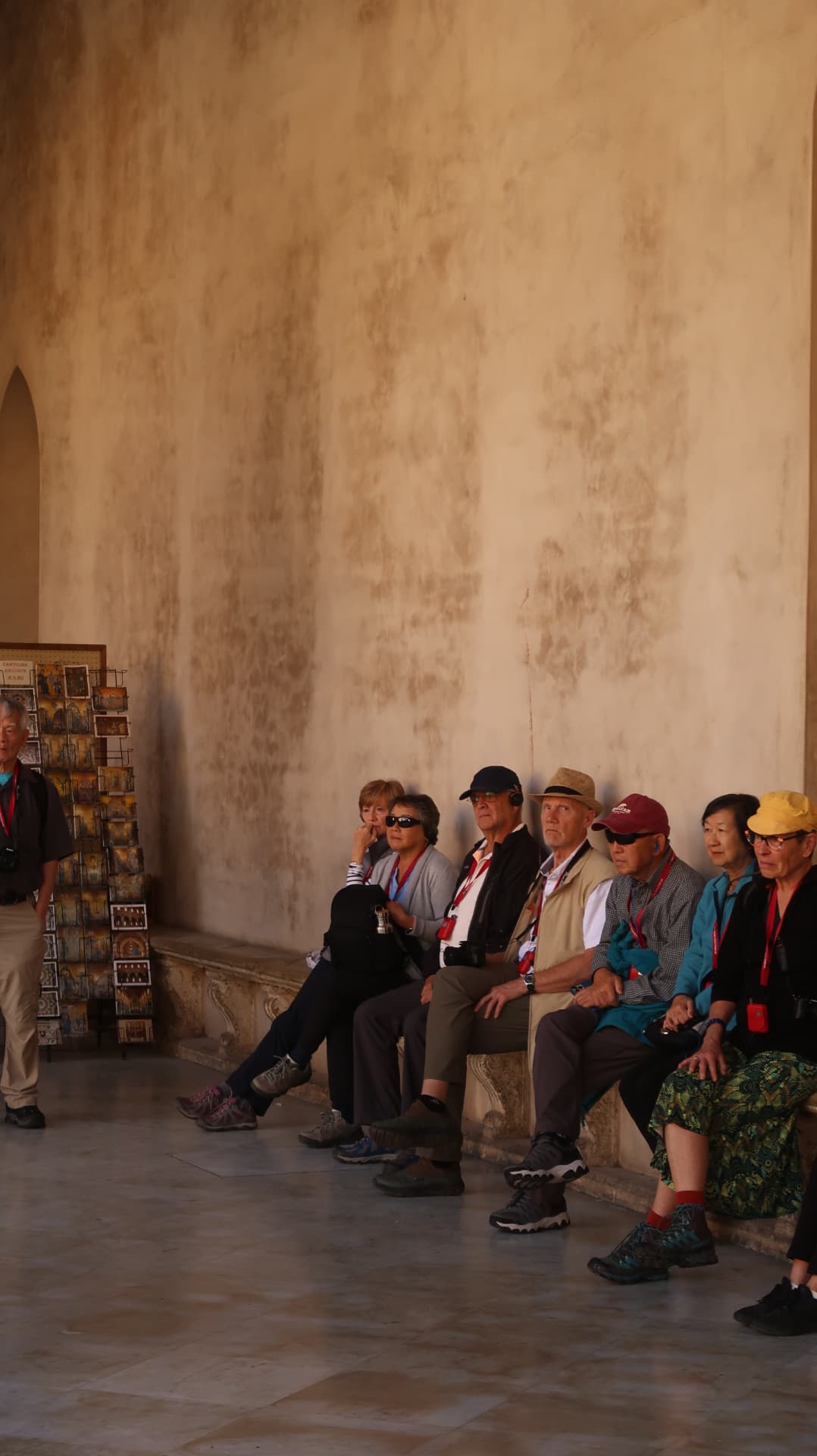 Tour group resting on a stone bench in a sunlit cloister