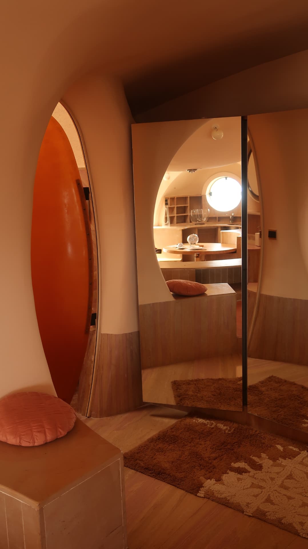 Orange oval door beside a mirrored panel reflecting a timber kitchen and porthole