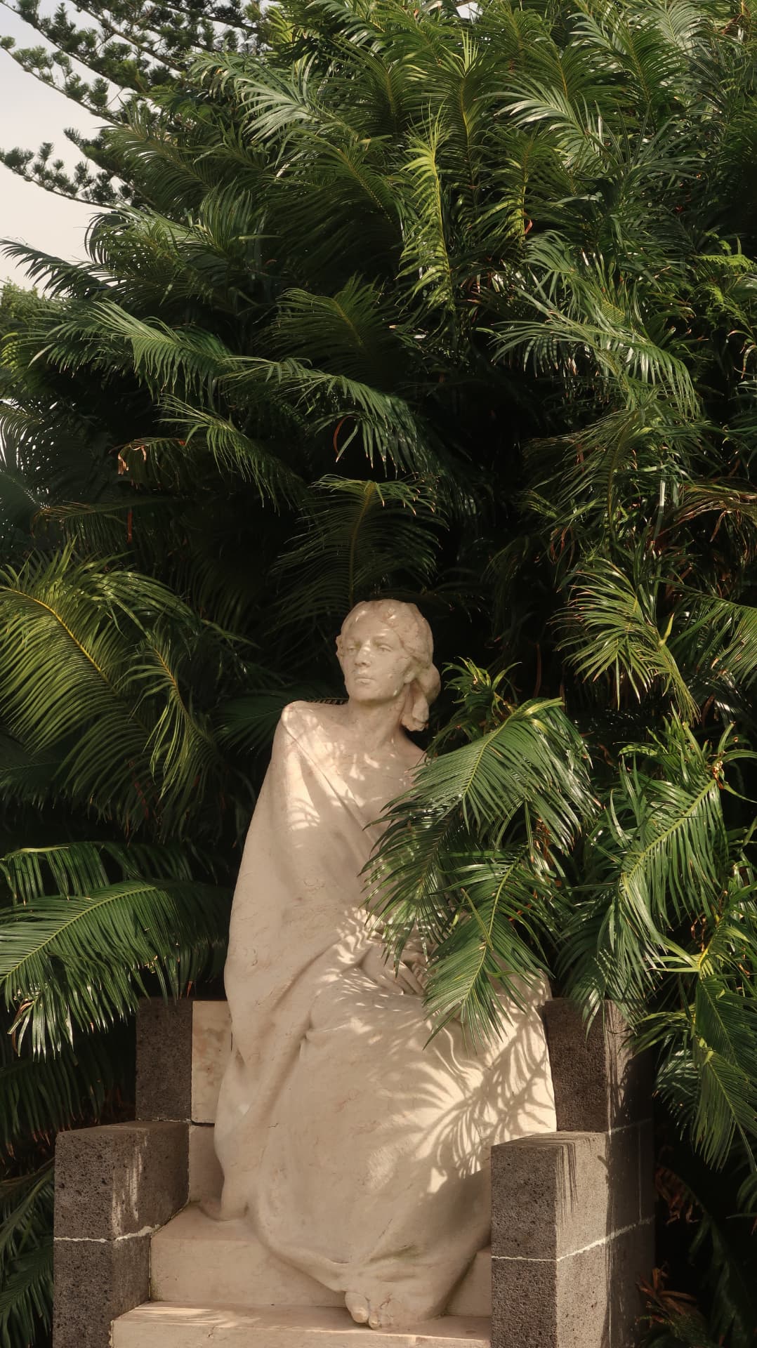 Marble seated figure among palm fronds with dappled shadow
