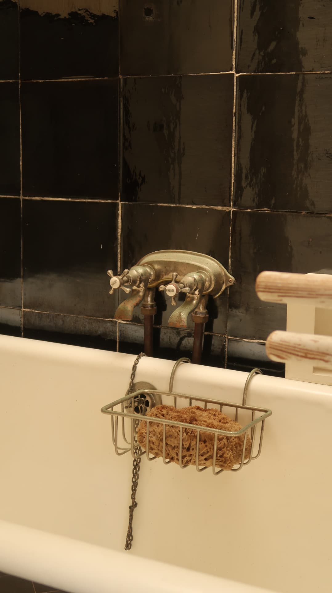 Brass taps and a wire basket with a sponge on a white bath