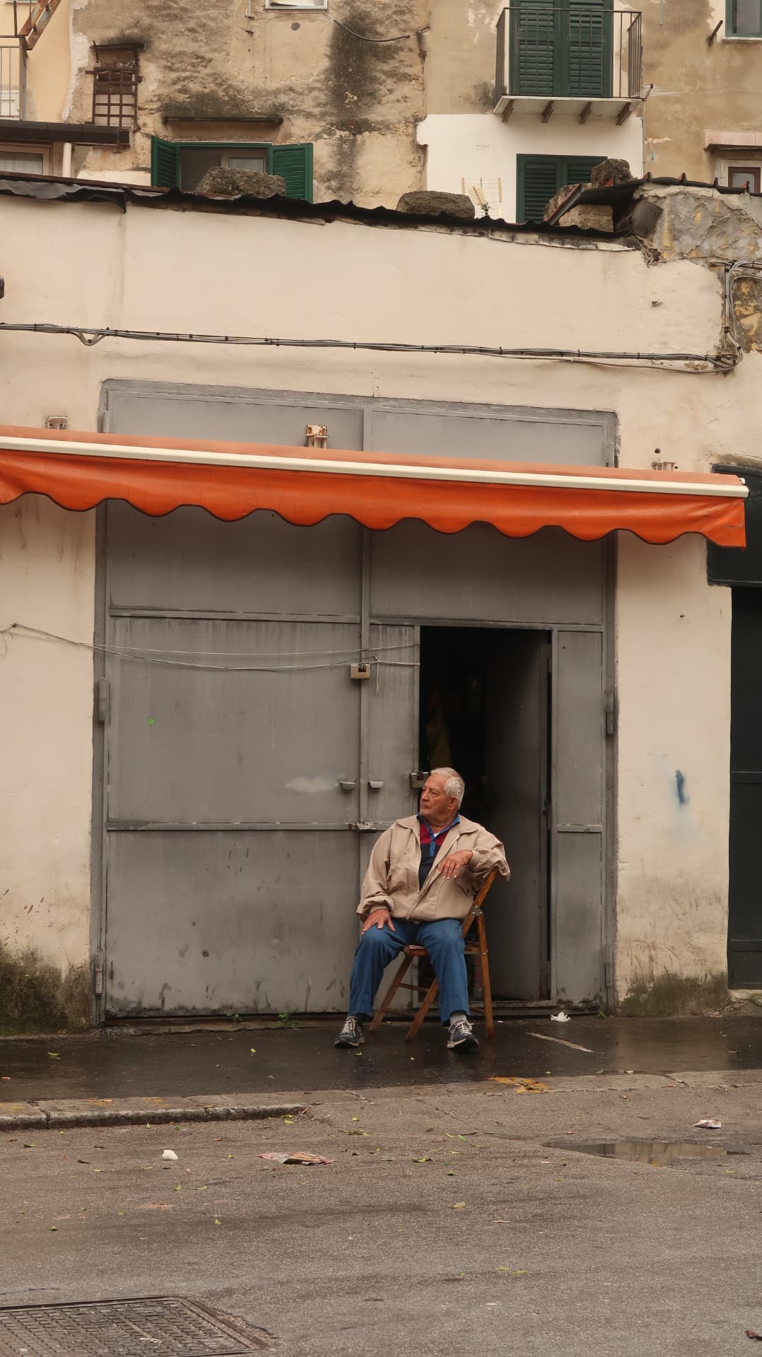 Man seated alone beneath a long orange awning on a grey shopfront
