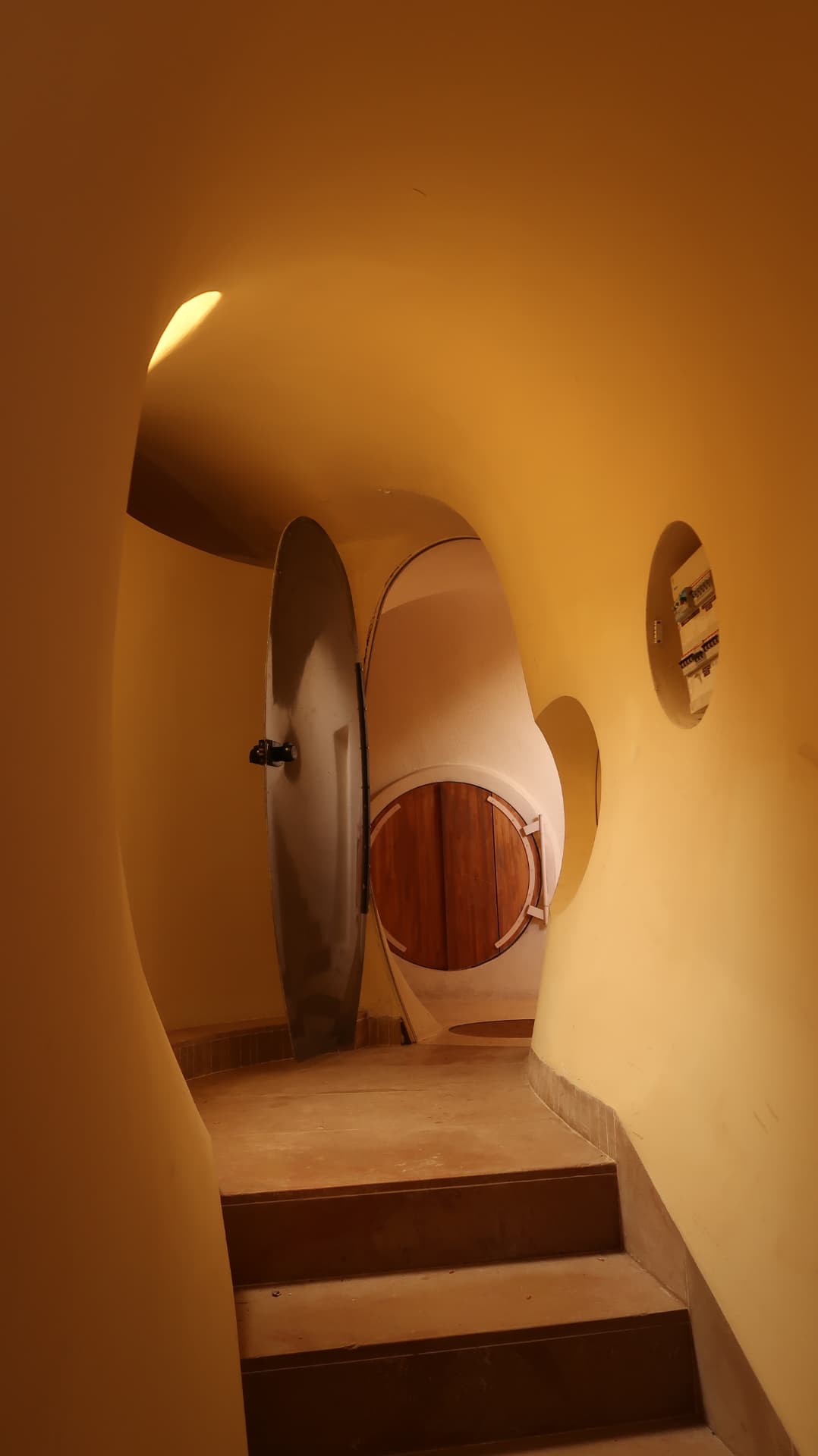 Amber lit stair landing with an oval steel door and round wooden hatch