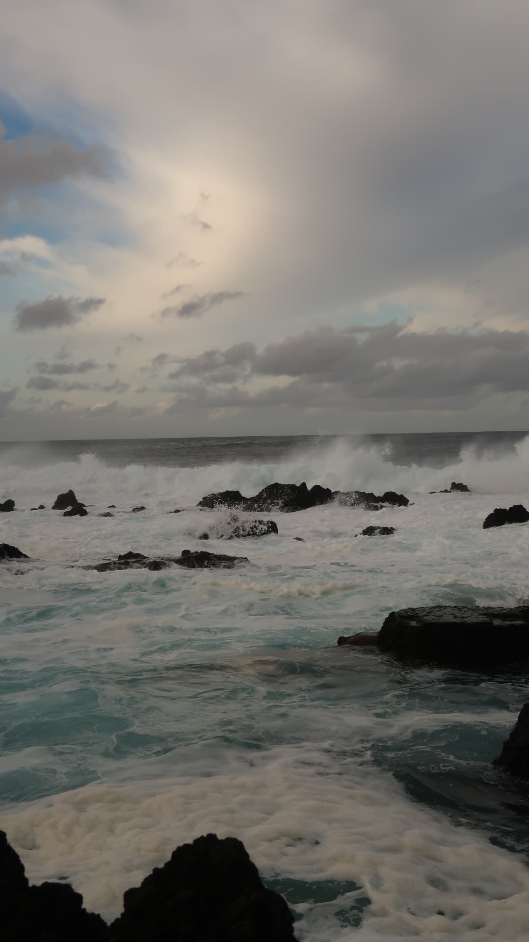 Waves breaking over black lava rocks under a pale sky