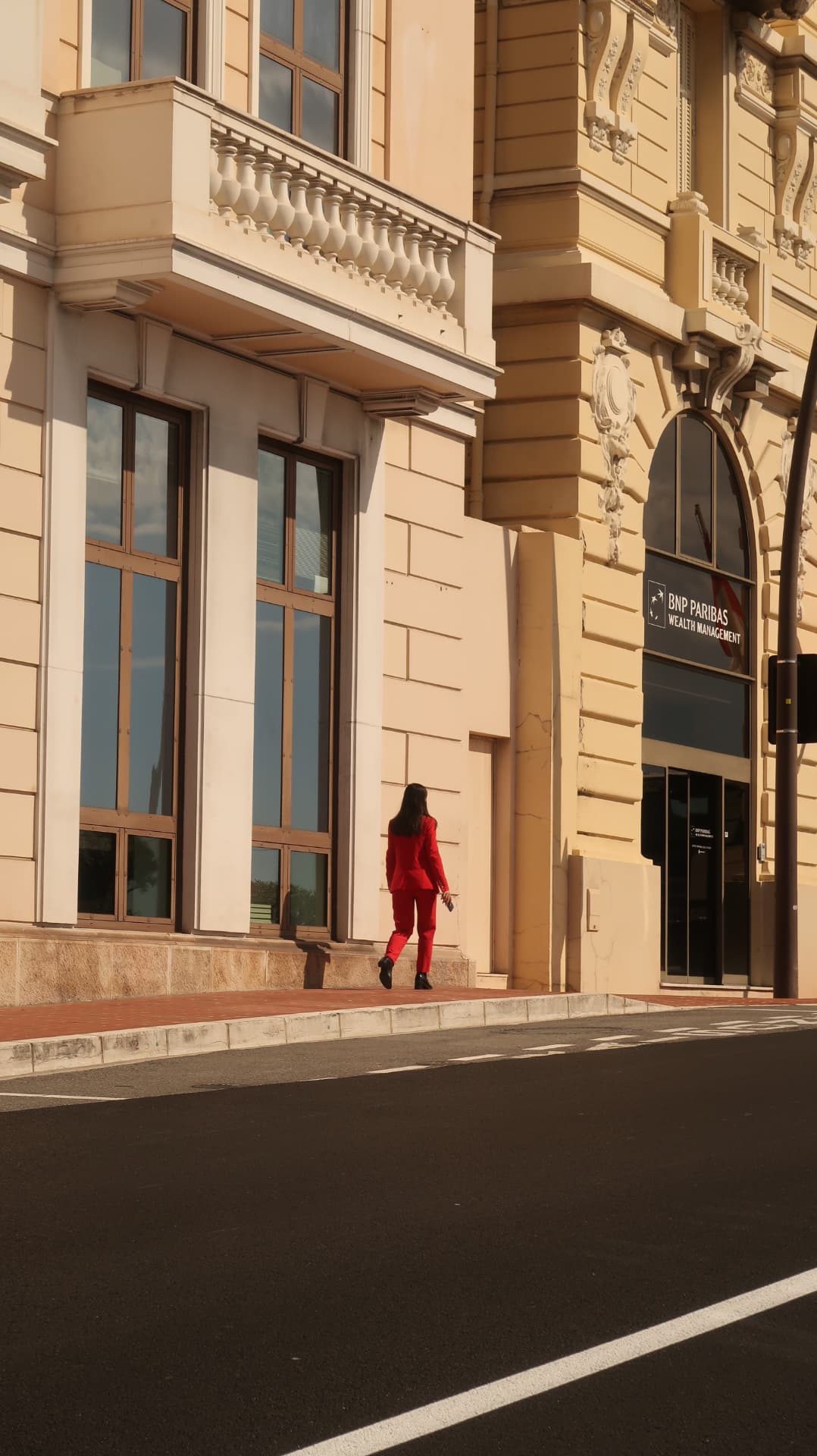 Woman in a red suit crossing a sunlit stone facade