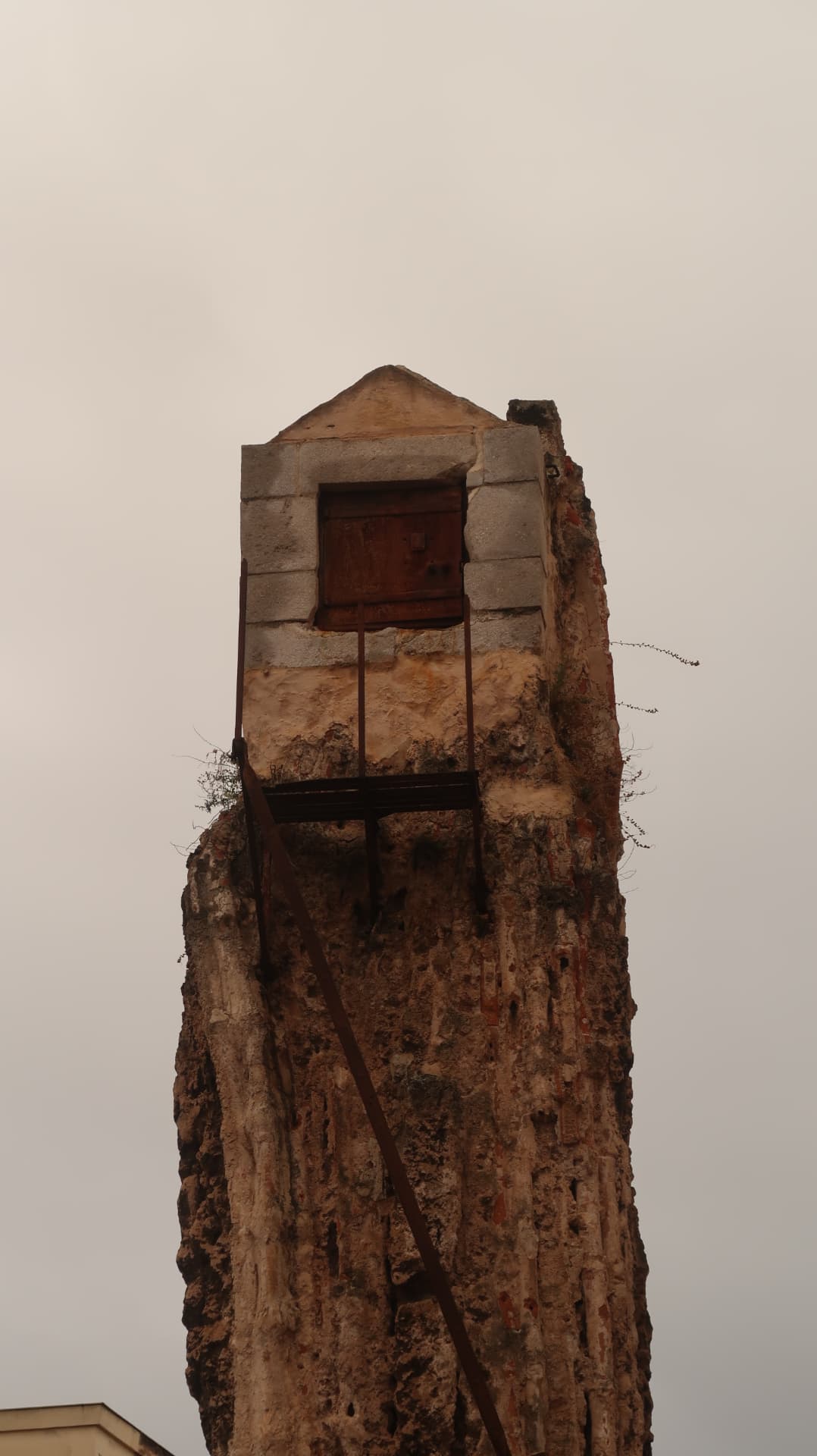 Ruined wall fragment with a shuttered niche against a pale sky