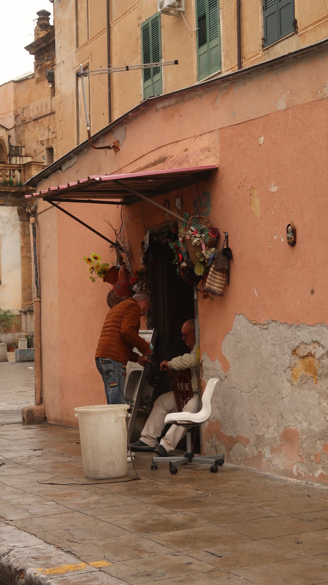 Two men moving chairs in a doorway of a pink stucco corner house