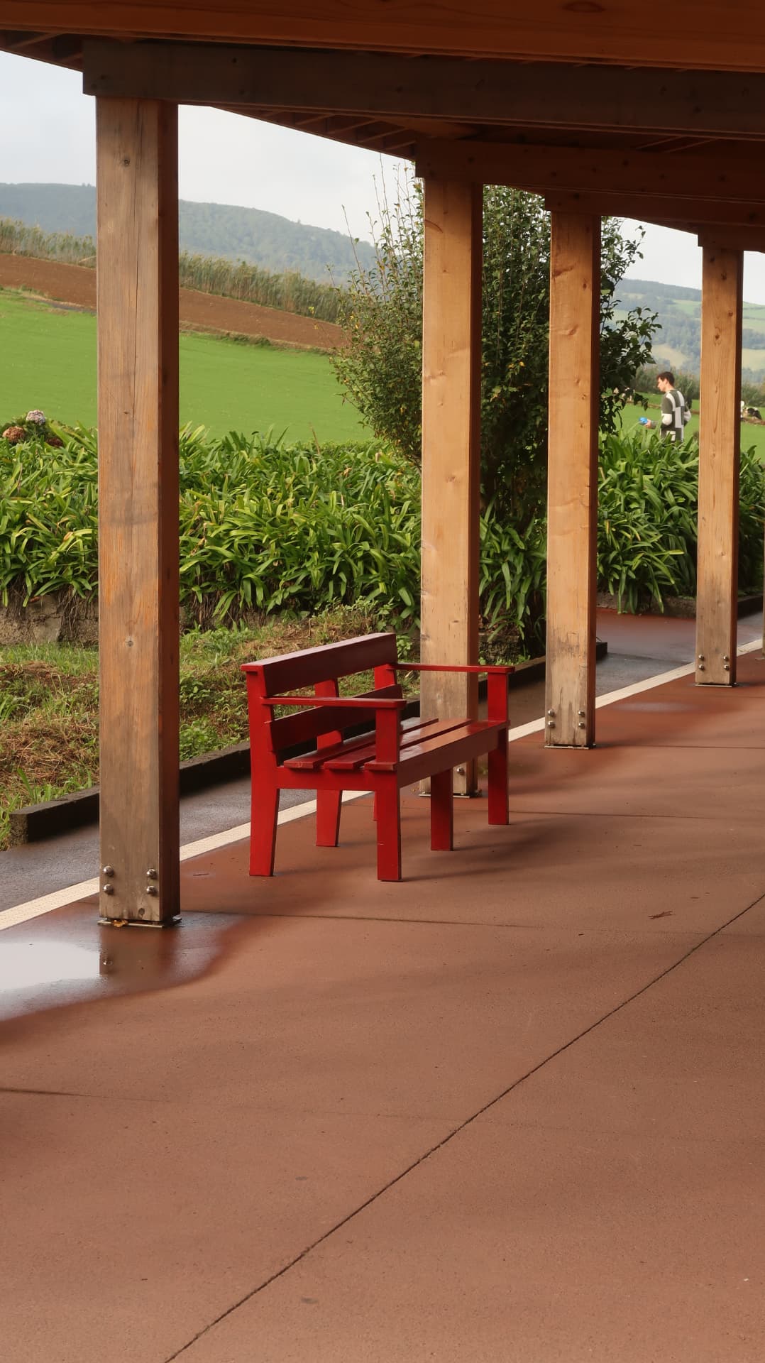 Red bench under a timber colonnade facing green fields