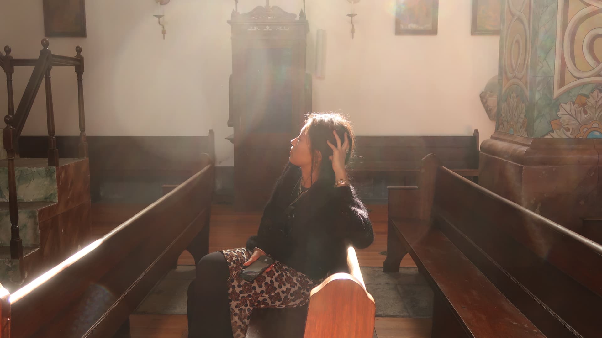Woman seated in a church pew looking up into a shaft of light