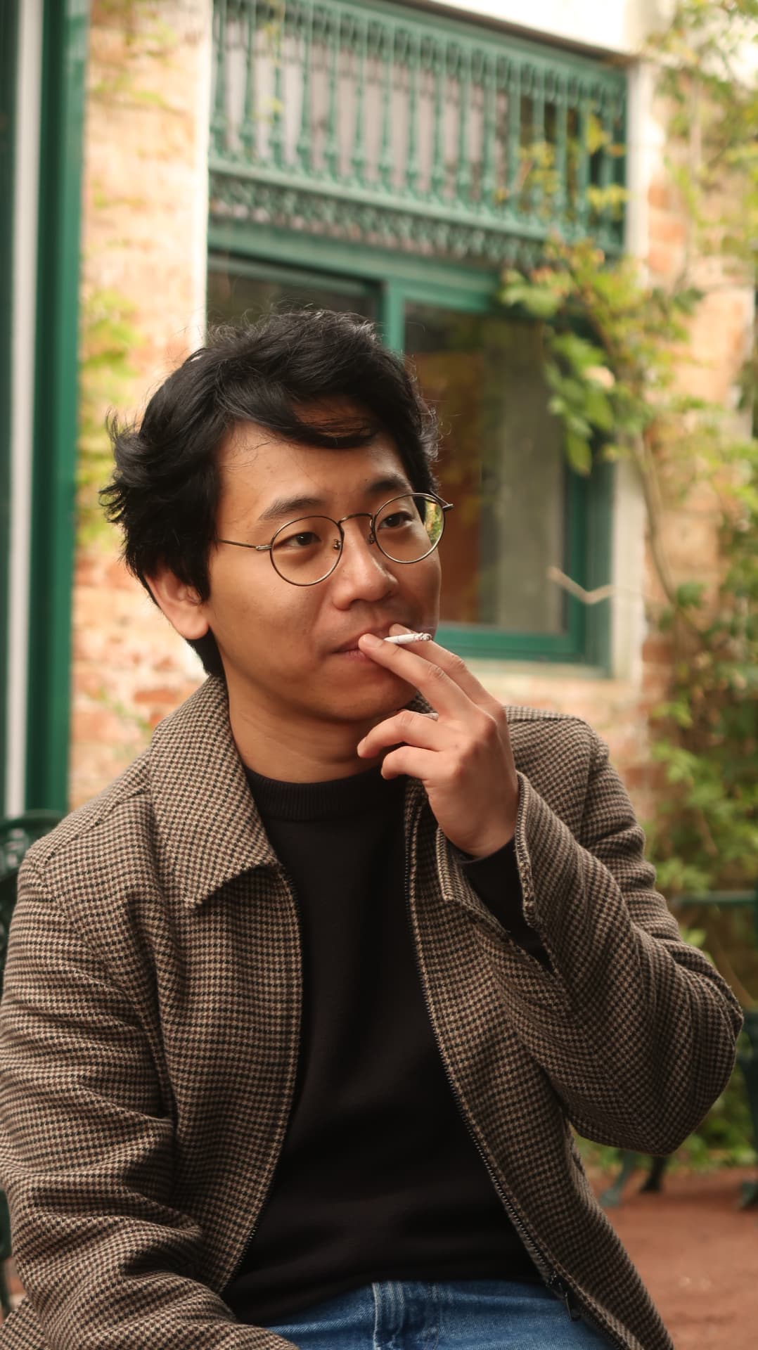 Man in a houndstooth jacket smoking outside a green framed window