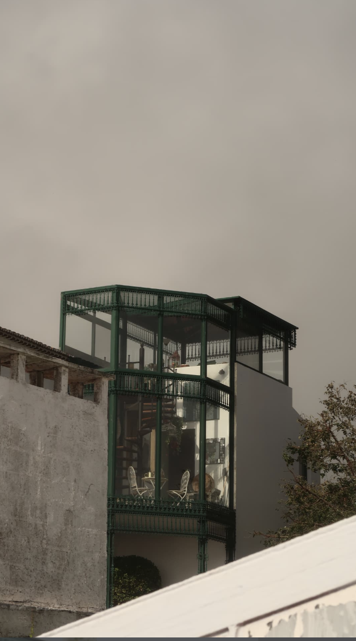 A green metal-framed glass tower rising above whitewashed walls under an overcast sky