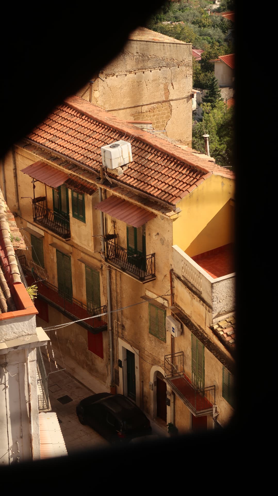 Ochre houses with green shutters and tiled roofs glimpsed through a window