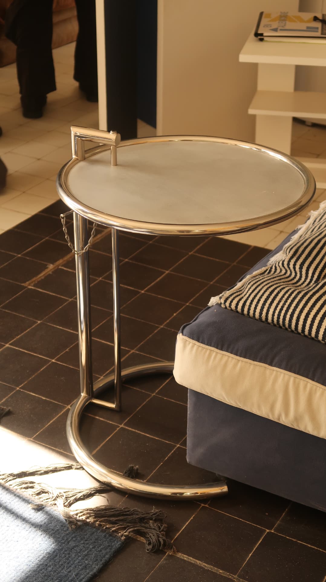 Chrome and glass side table beside a low daybed on dark tiles