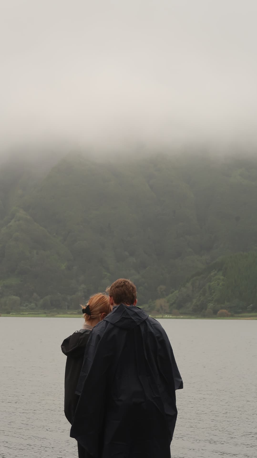 Two people in rain capes looking across a crater lake
