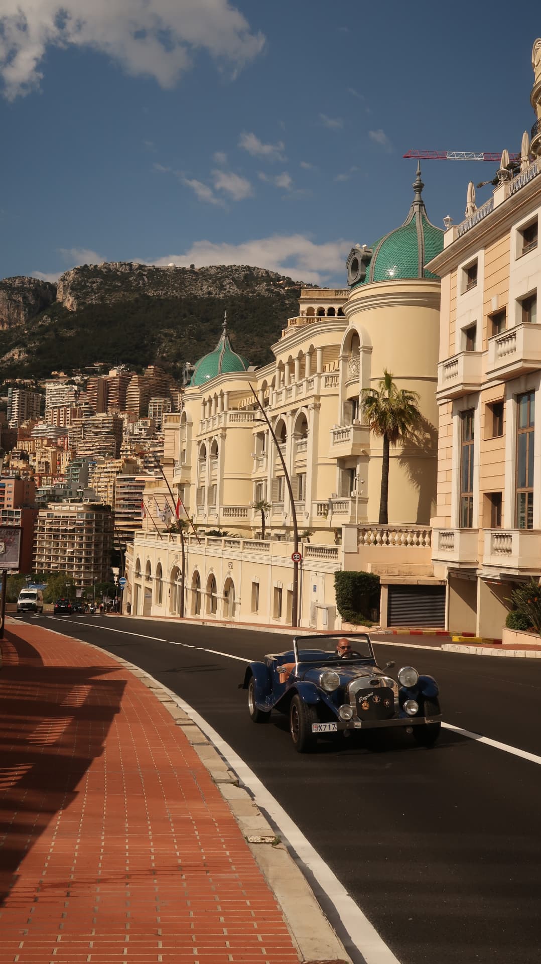 Blue roadster passing green domed Belle Époque facades