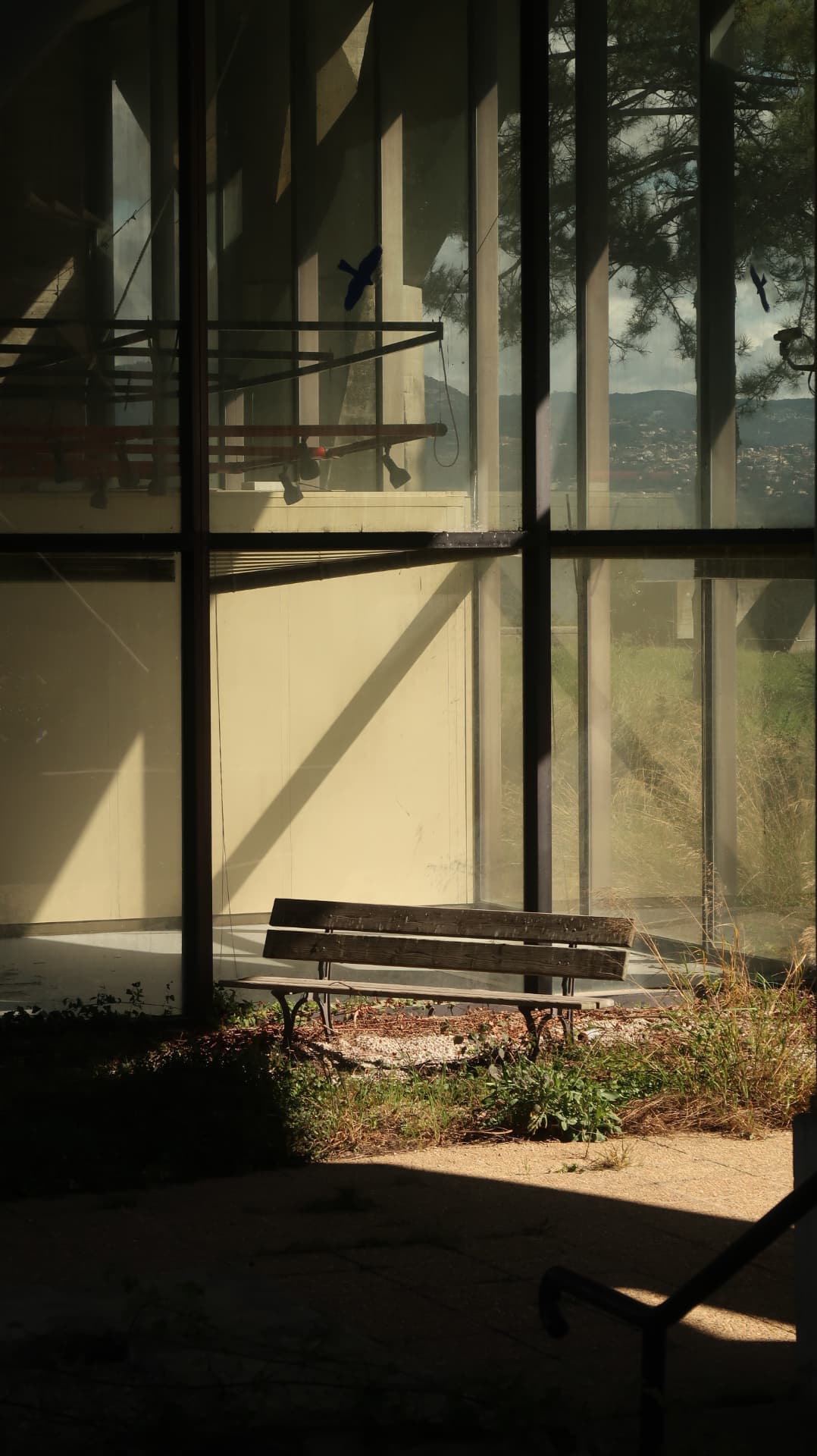 Empty bench behind a glass curtain wall with the hills of Nice beyond