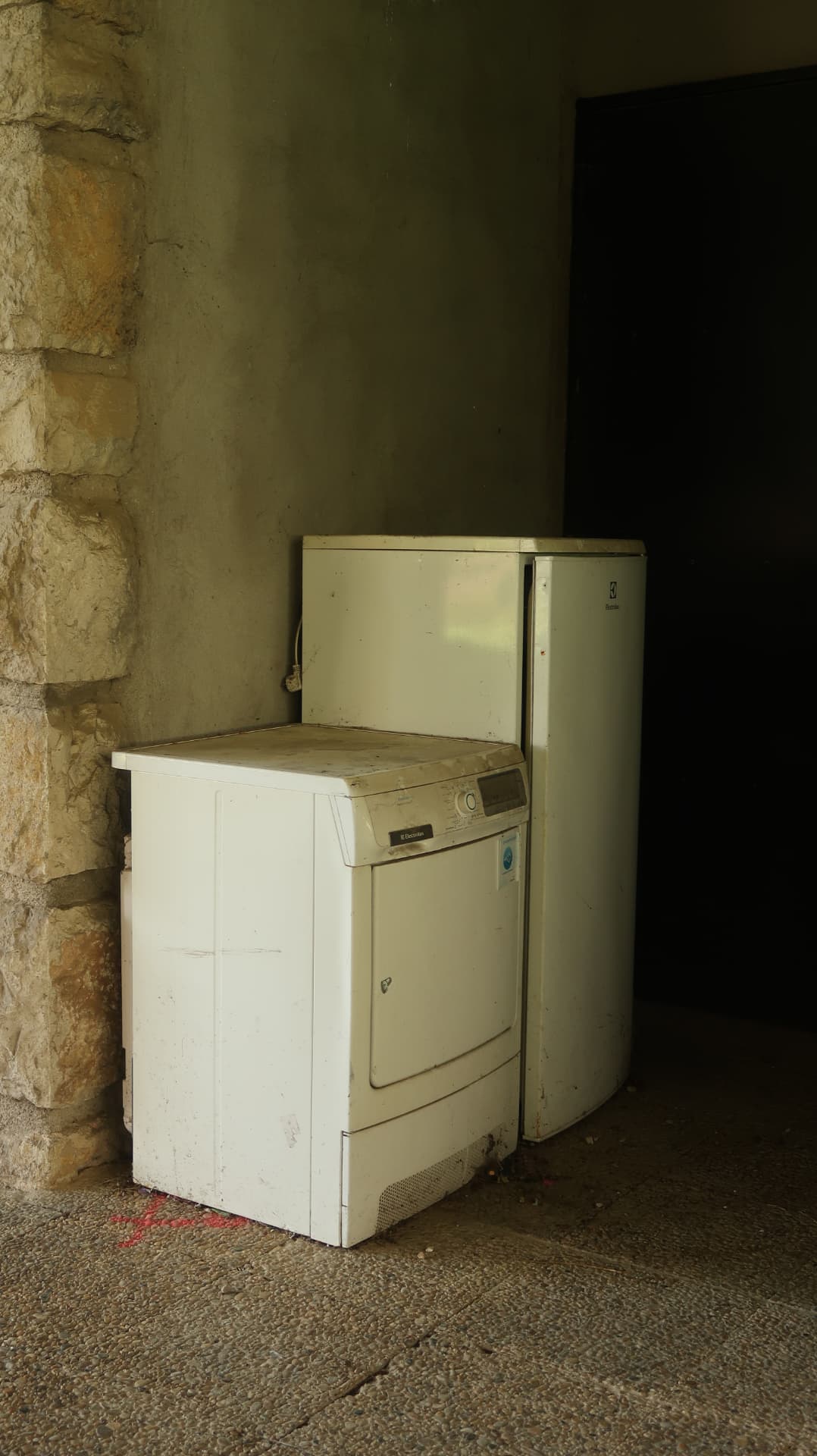 Abandoned washing machine and fridge in a stone corner