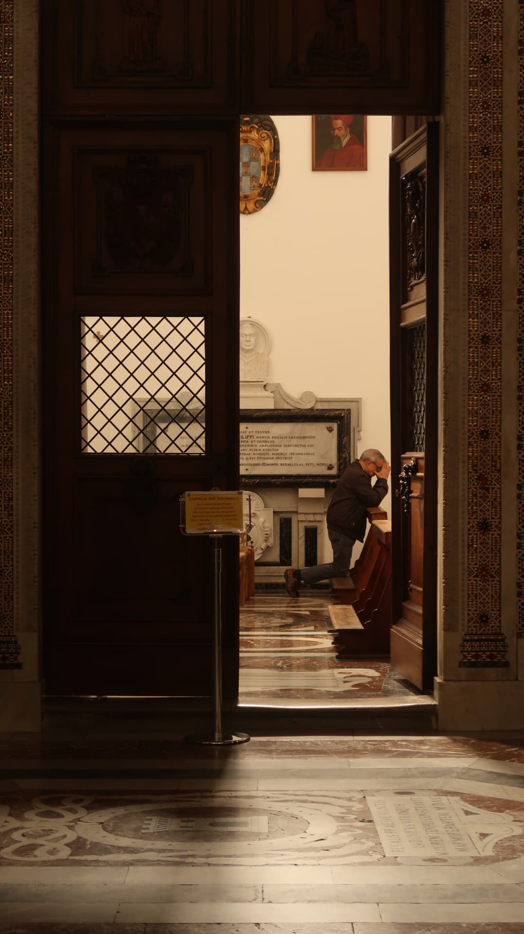 Man praying in a chapel seen through a dark carved doorway