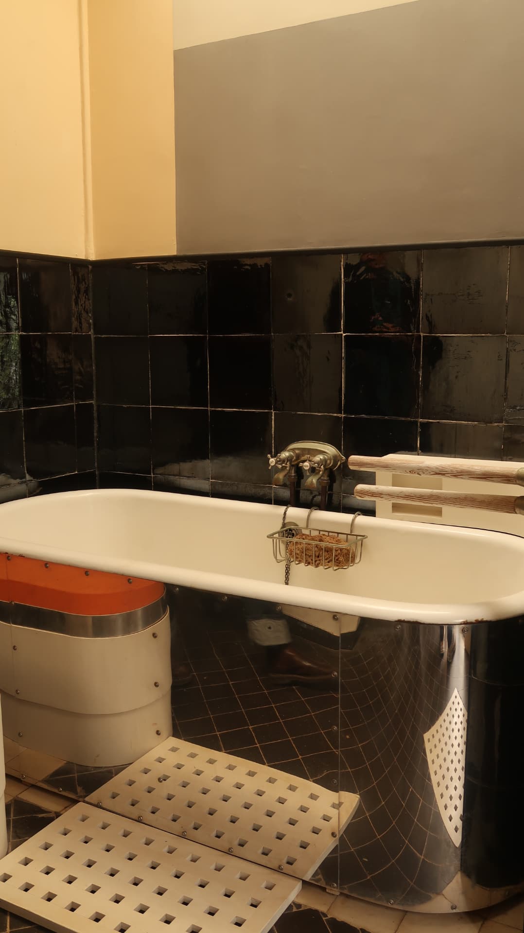 Freestanding bath against black glazed tiles with steel grates