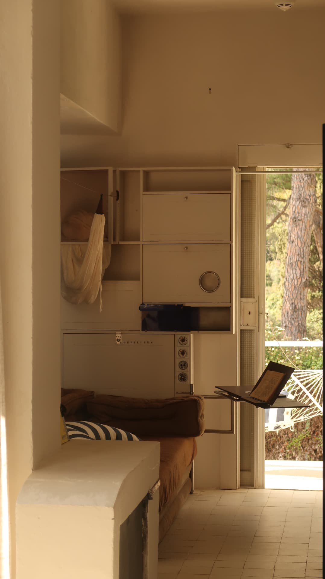 Built-in cabinetry and cot beside an open door onto pines
