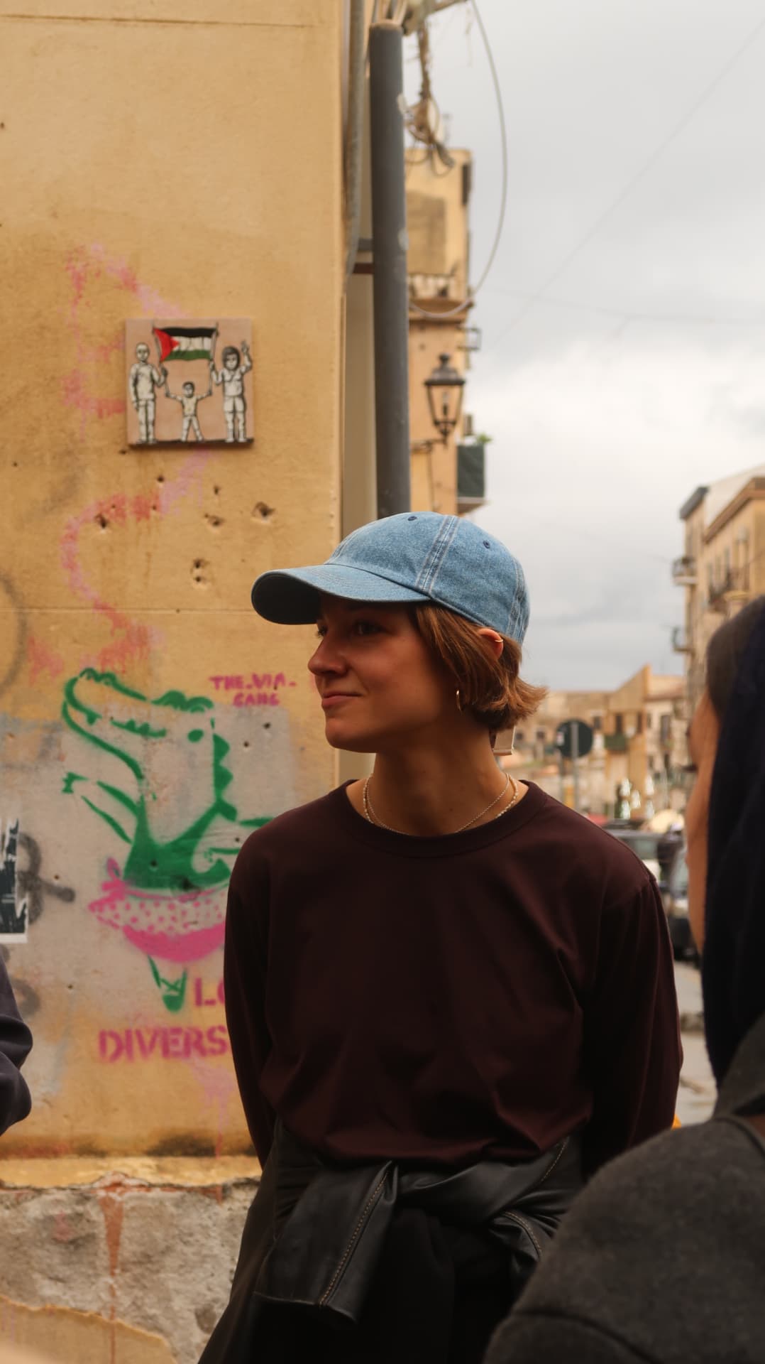 Woman in a denim cap beside a graffitied wall in a Palermo street