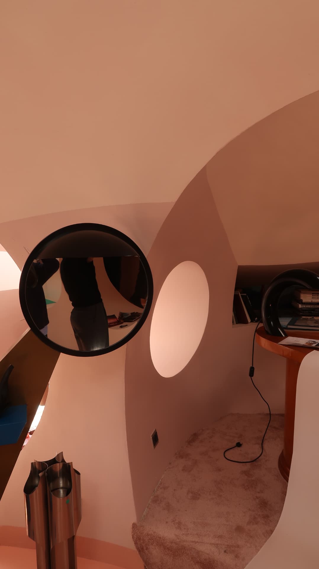 Convex black mirror on a curved blush wall beside a round opening