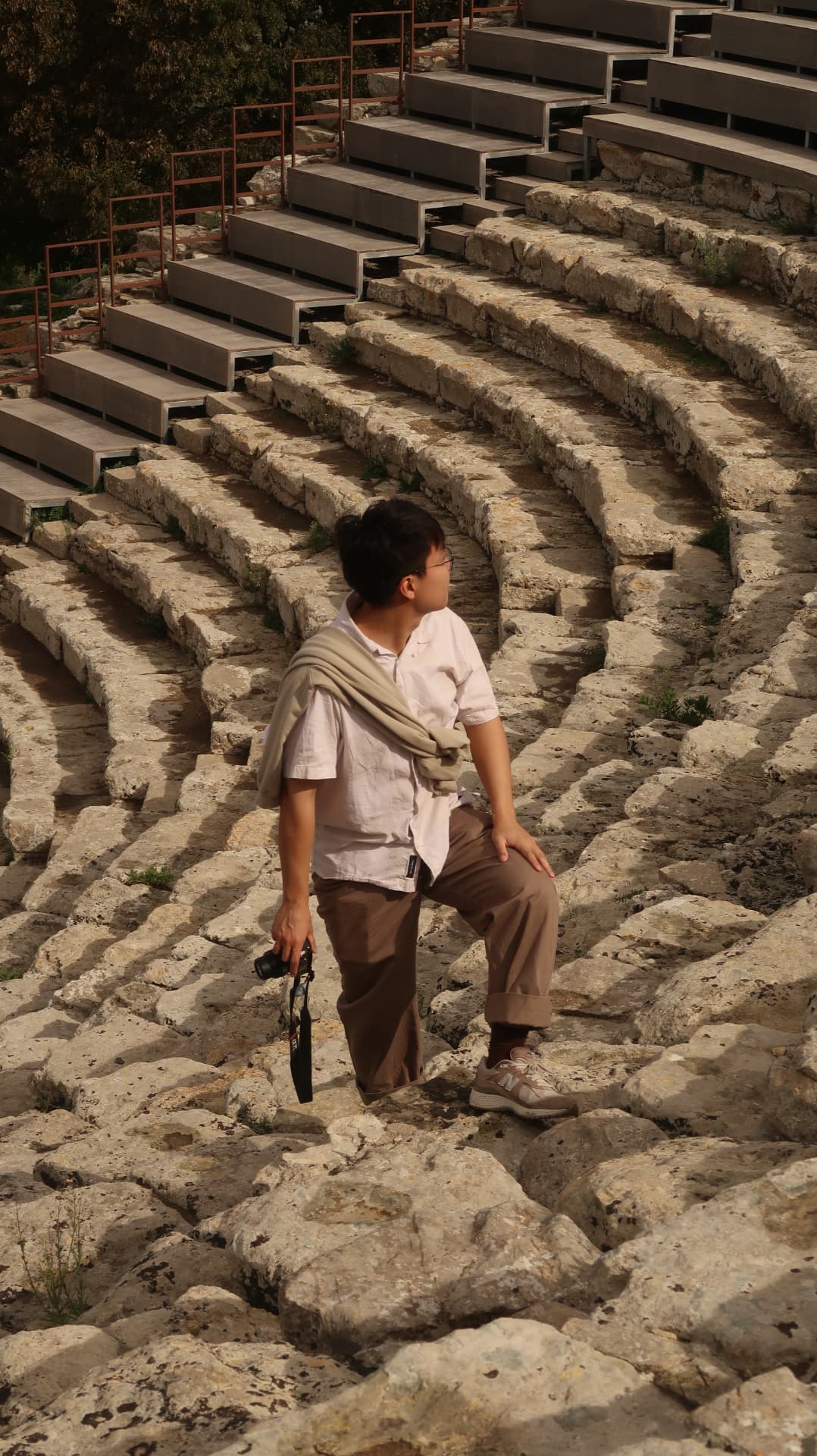 Visitor with a camera standing on the stone tiers of a Greek theatre