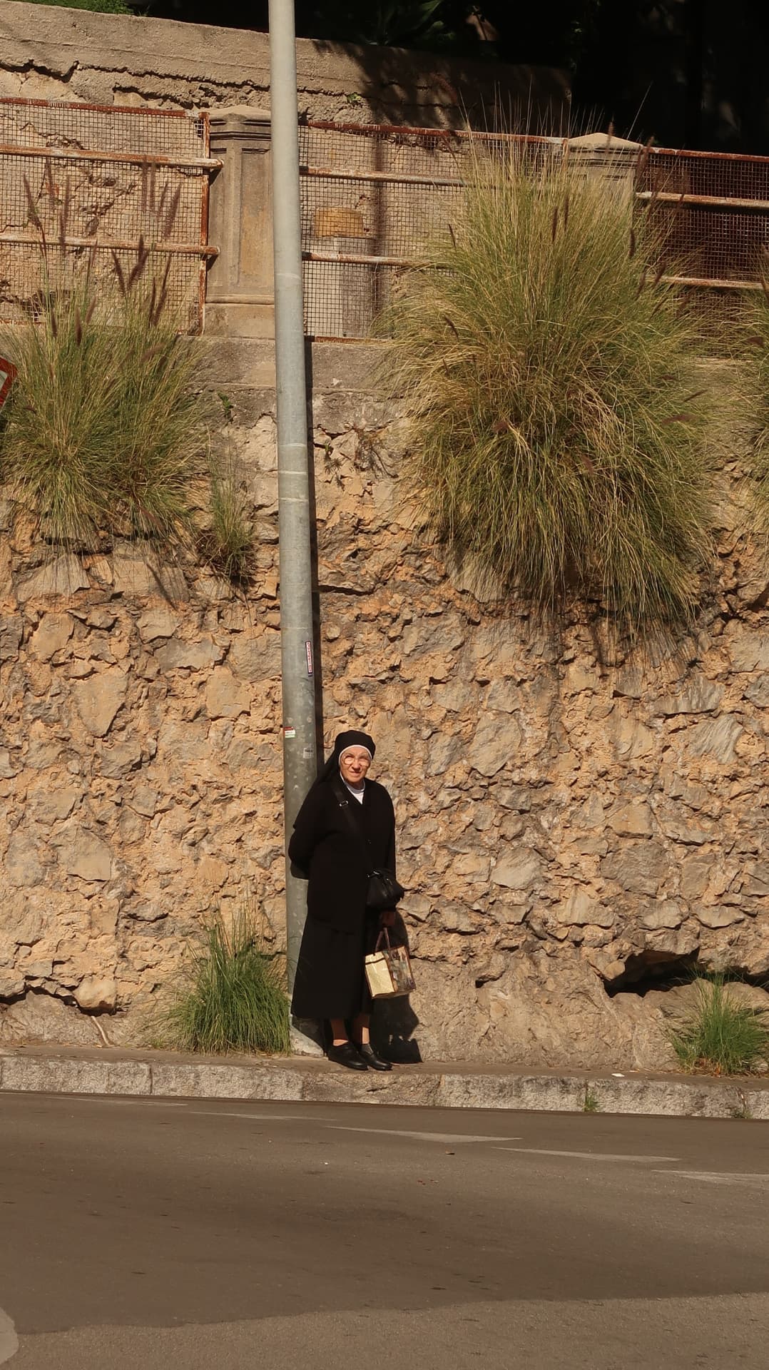 Nun waiting beside a lamppost against a dry stone wall