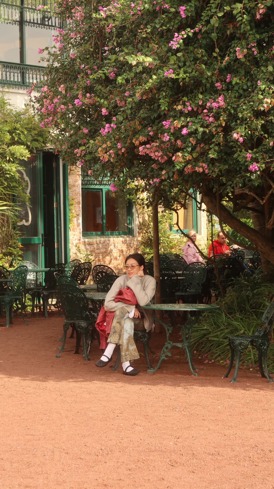 Woman seated at a garden cafe table under a flowering bougainvillea