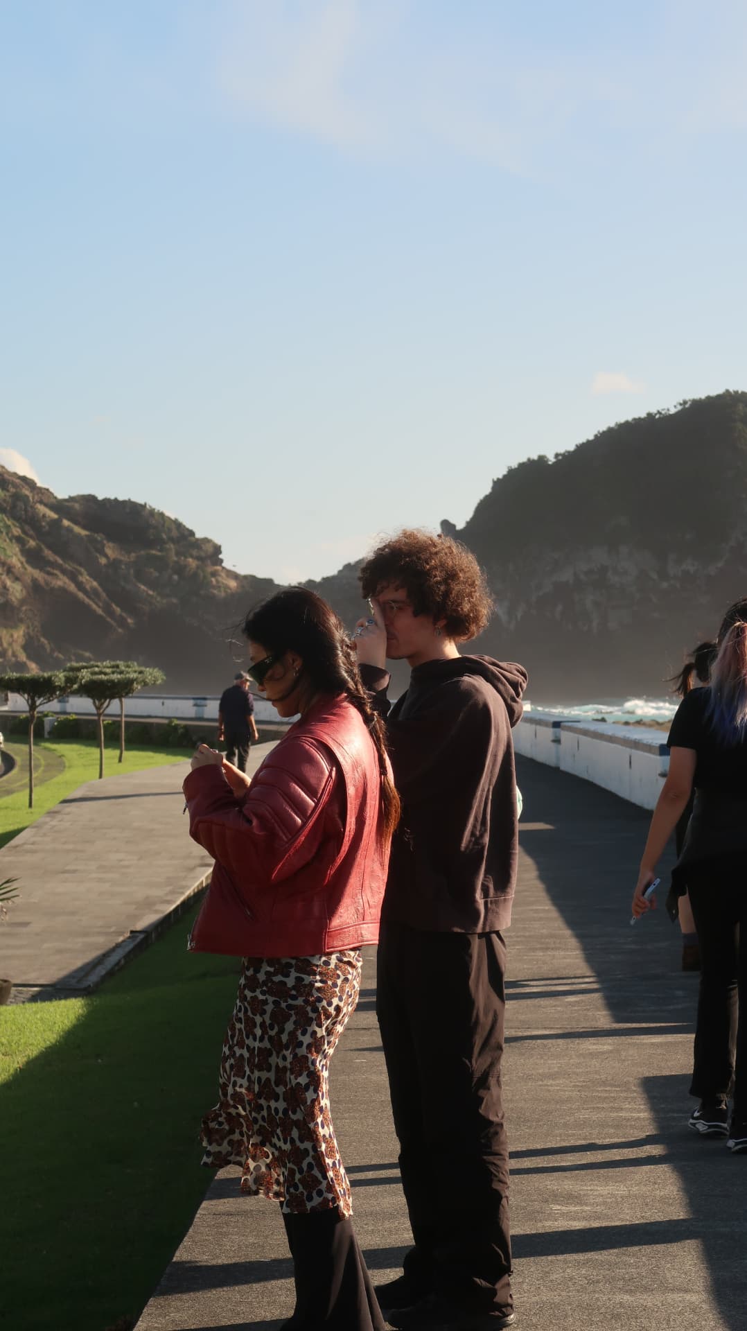 Two people on a seafront promenade below green headlands