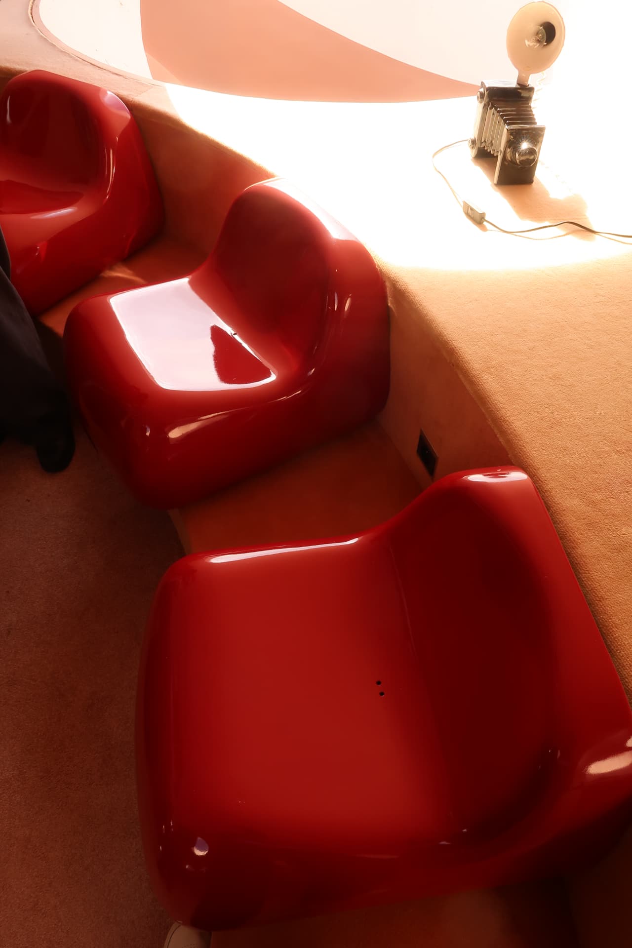 Three glossy red moulded armchairs on sand coloured carpet