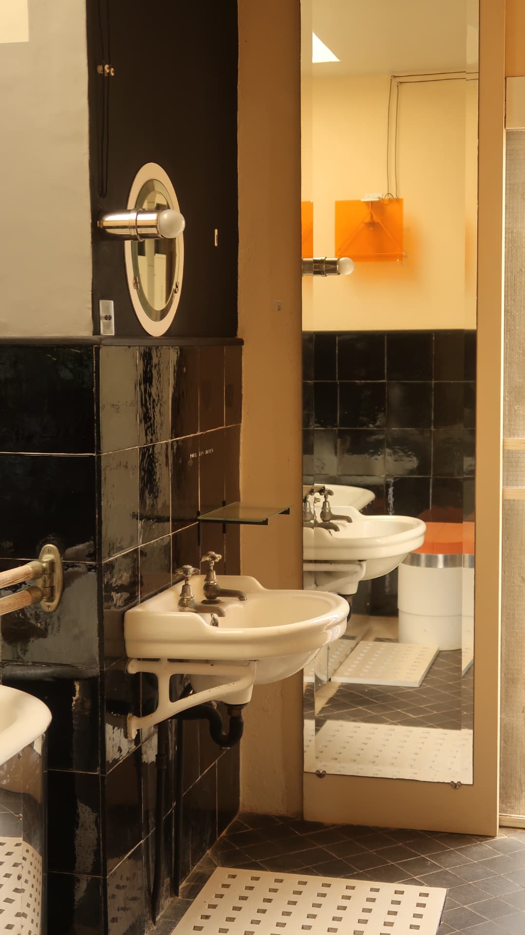 Black tiled washroom with two basins and a mirrored door