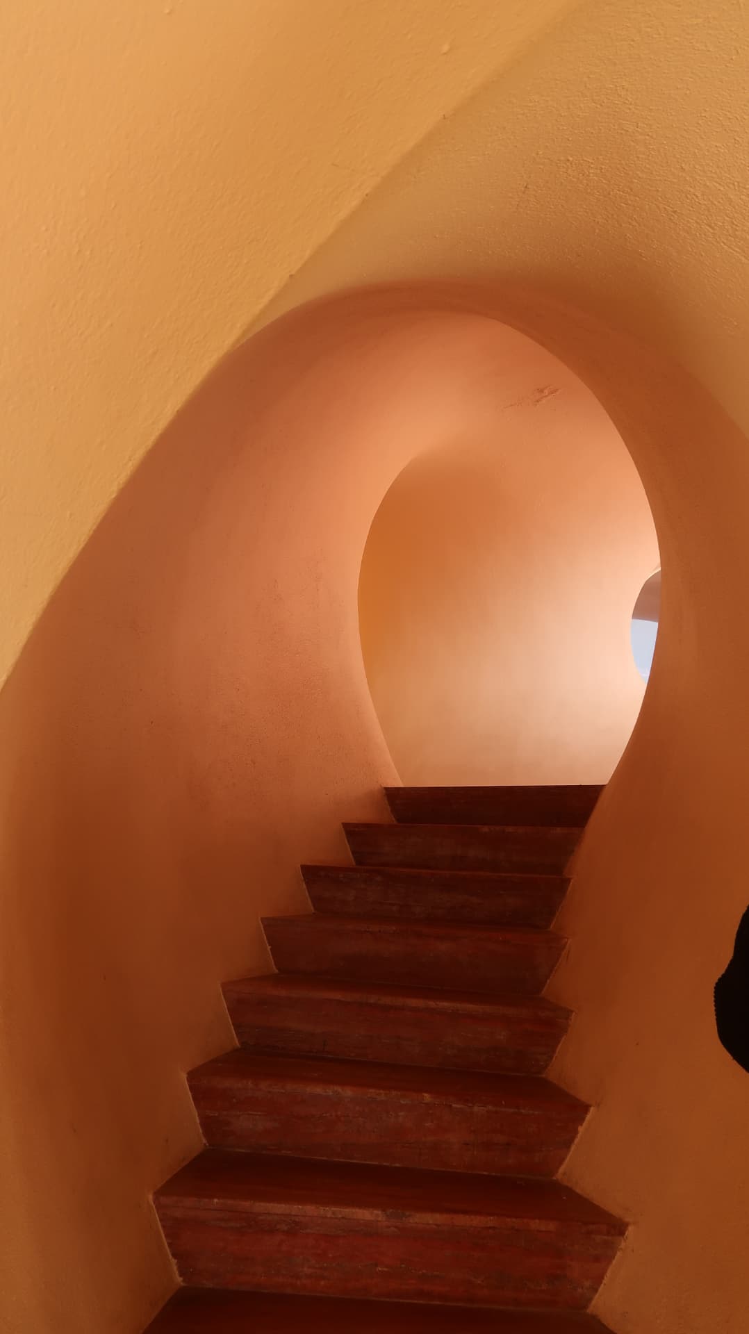 Stairway rising through a rounded apricot tunnel toward a circular opening