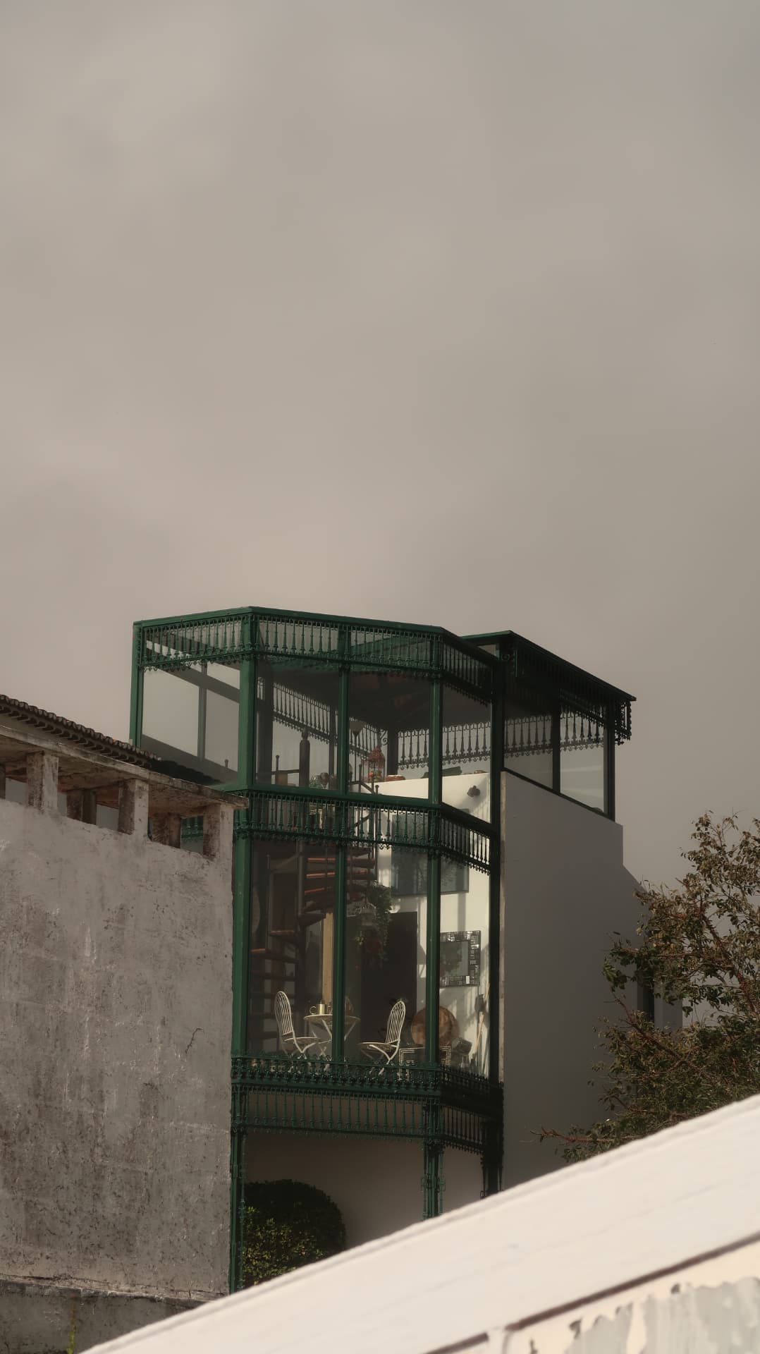 Green iron and glass veranda rising above a concrete wall in mist