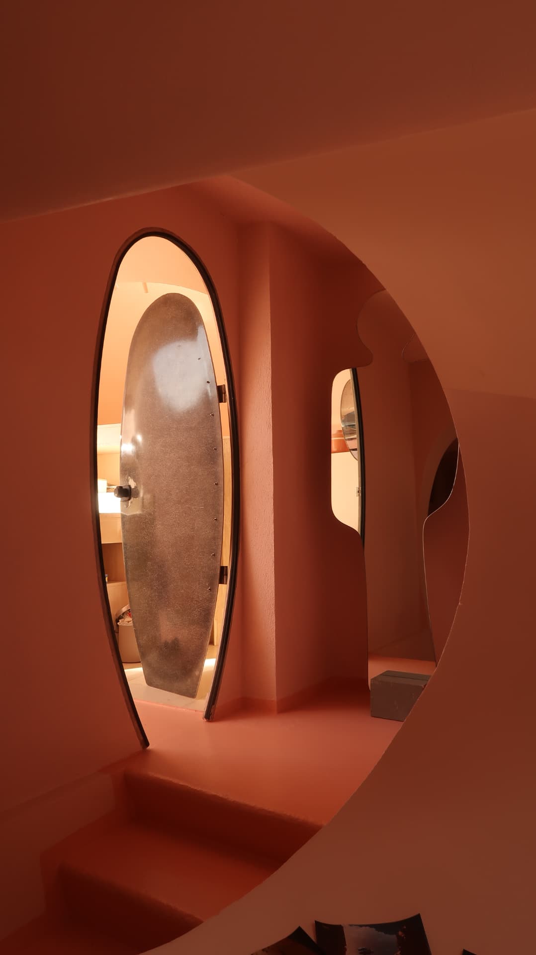 Oval metal door in a terracotta corridor with a circular cut through the wall