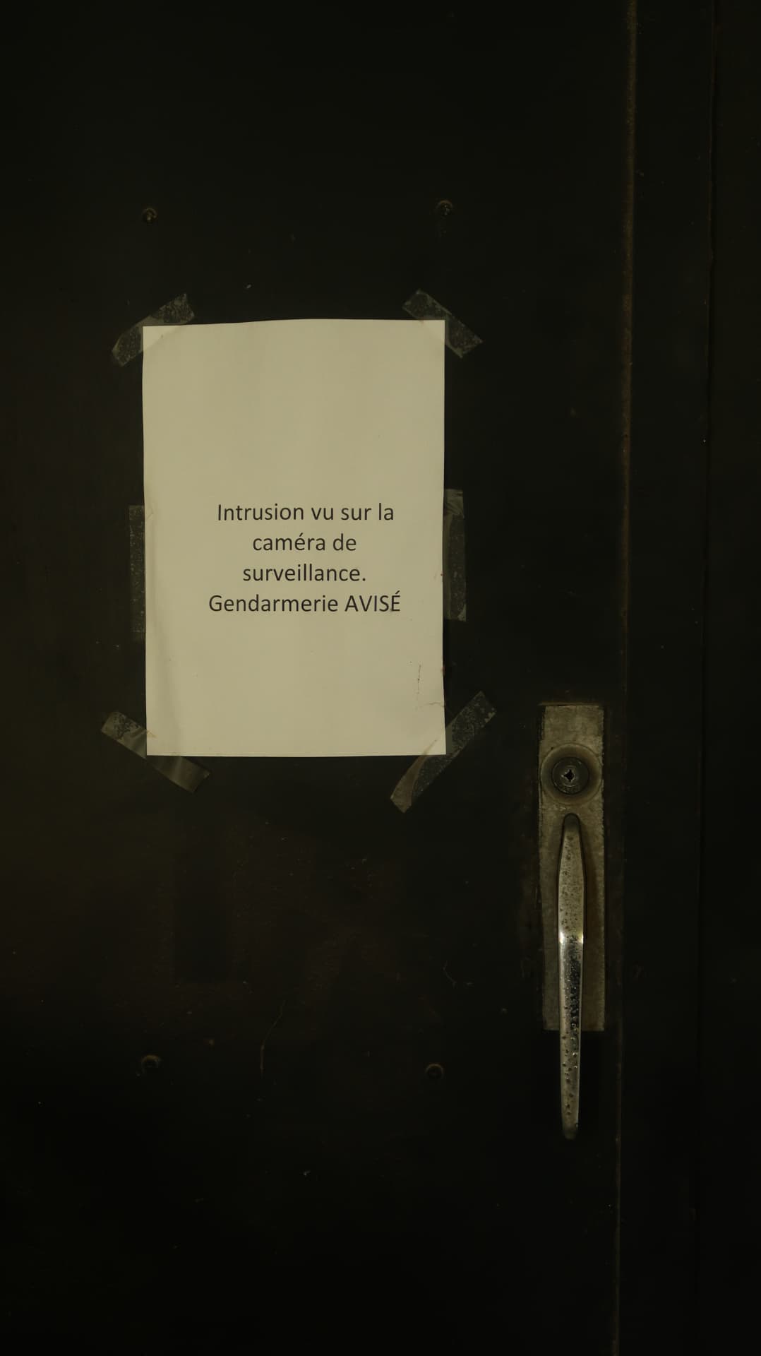 Taped notice about surveillance on a dark steel door