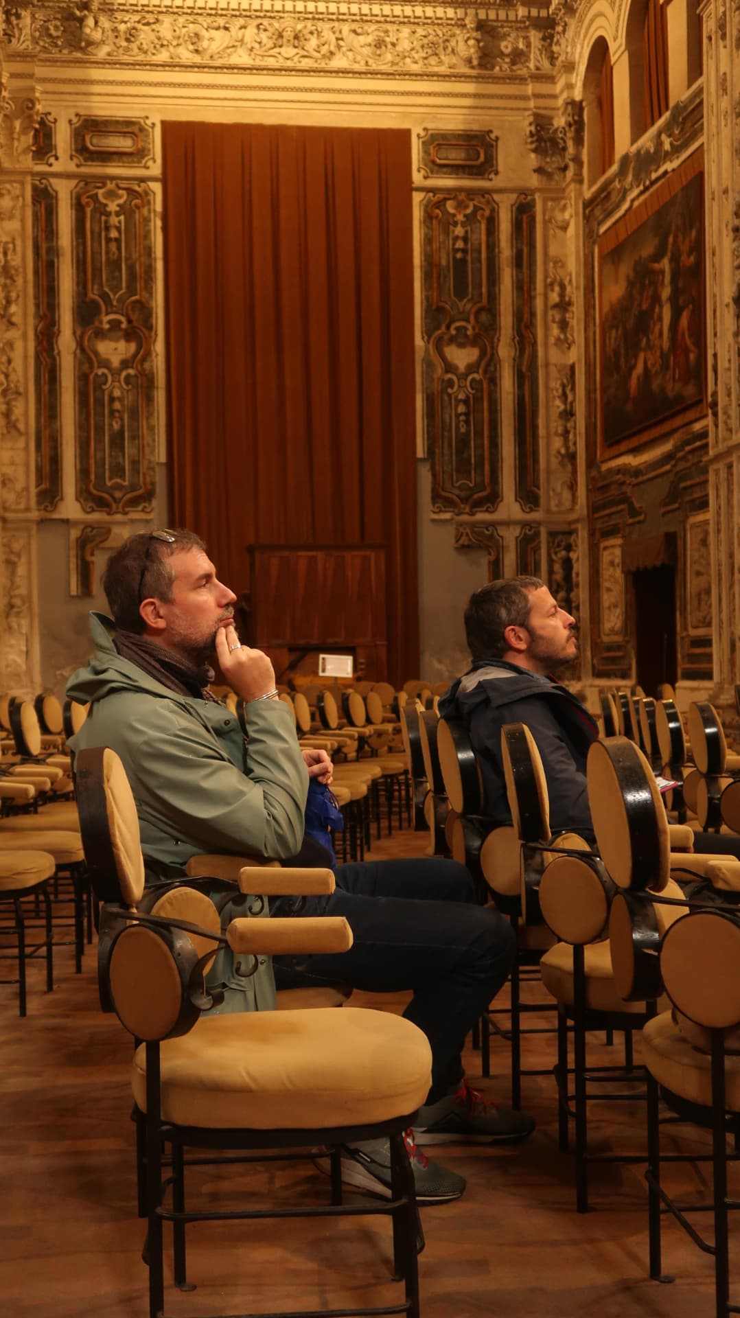 Two visitors seated in a frescoed hall looking upward